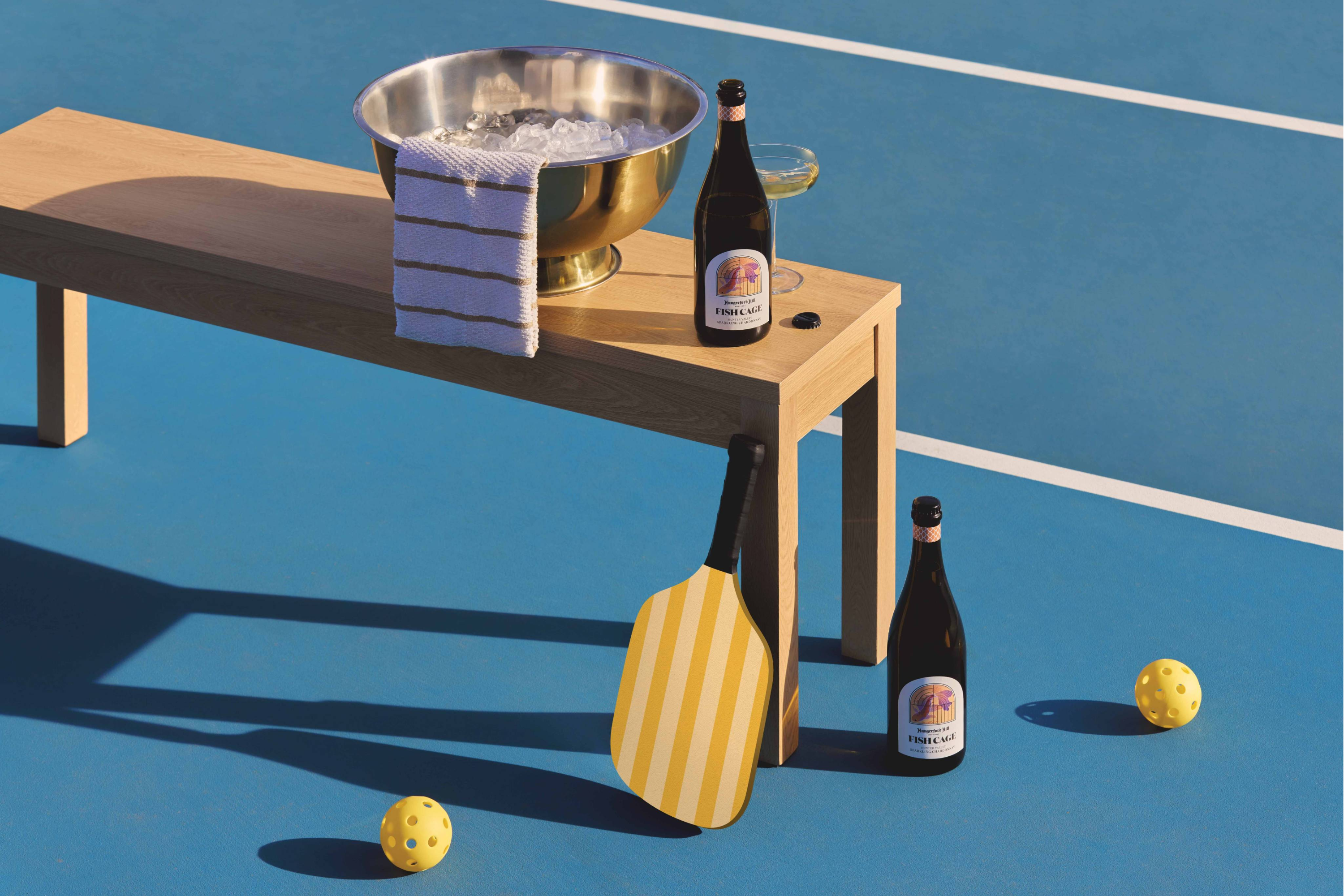 Tennis court with a wooden bench, pickleball equipment, and bottles.